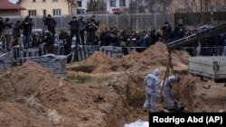 Работники кладбища эксгумируют труп мирного жителя, убитого в Буче, из братской могилы на окраине Киева, 13 апреля 2022 года